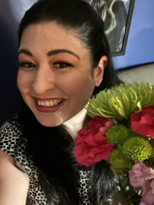 Photo of Liz Hernandex smiling, looking at the camera, holding some flowers